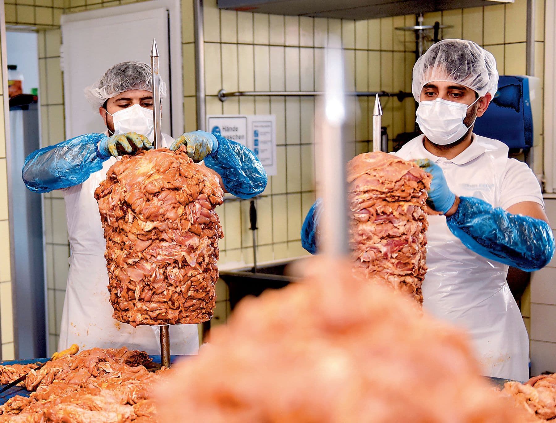 Zwei Mitarbeiter schichten in der Produktion Fleisch auf Dönerspiesse