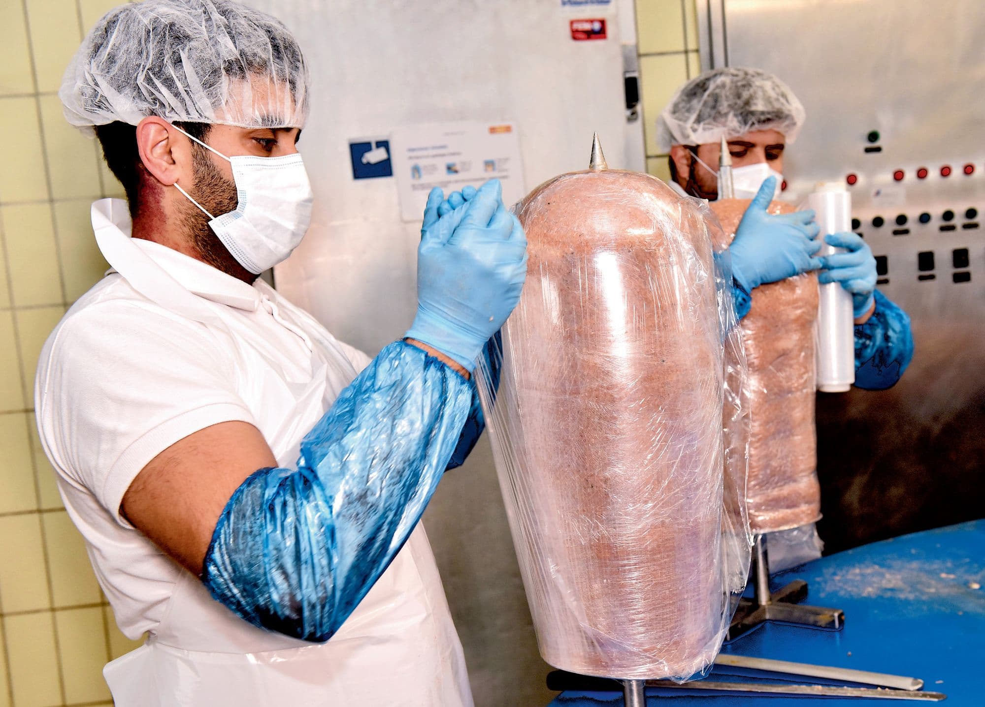 Ein Mitarbeiter verpackt einen Dönerspiess in Folie